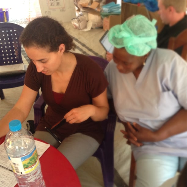 Two health workers sit together going through notes, one wearing a surgical cap.