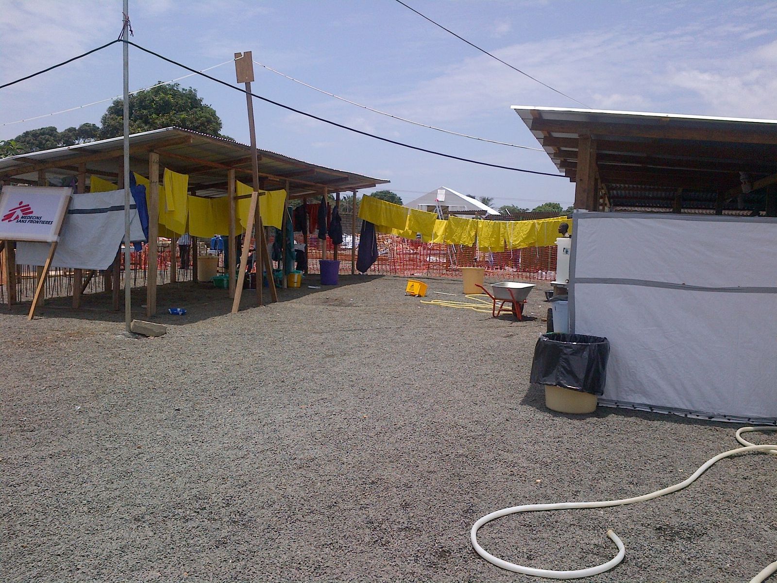 Open-sided tents and protective clothing hung out to dry at an Ebola treatment unit on gravel ground.