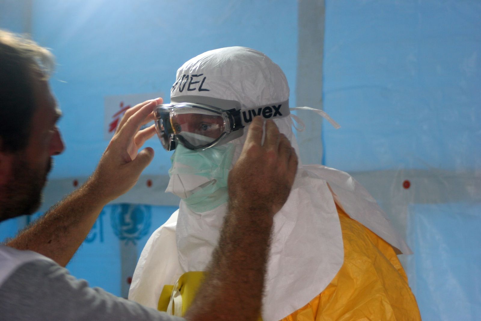 A health worker in a full protective suit and goggles has his goggles adjusted by a colleague before entering a treatment unit.