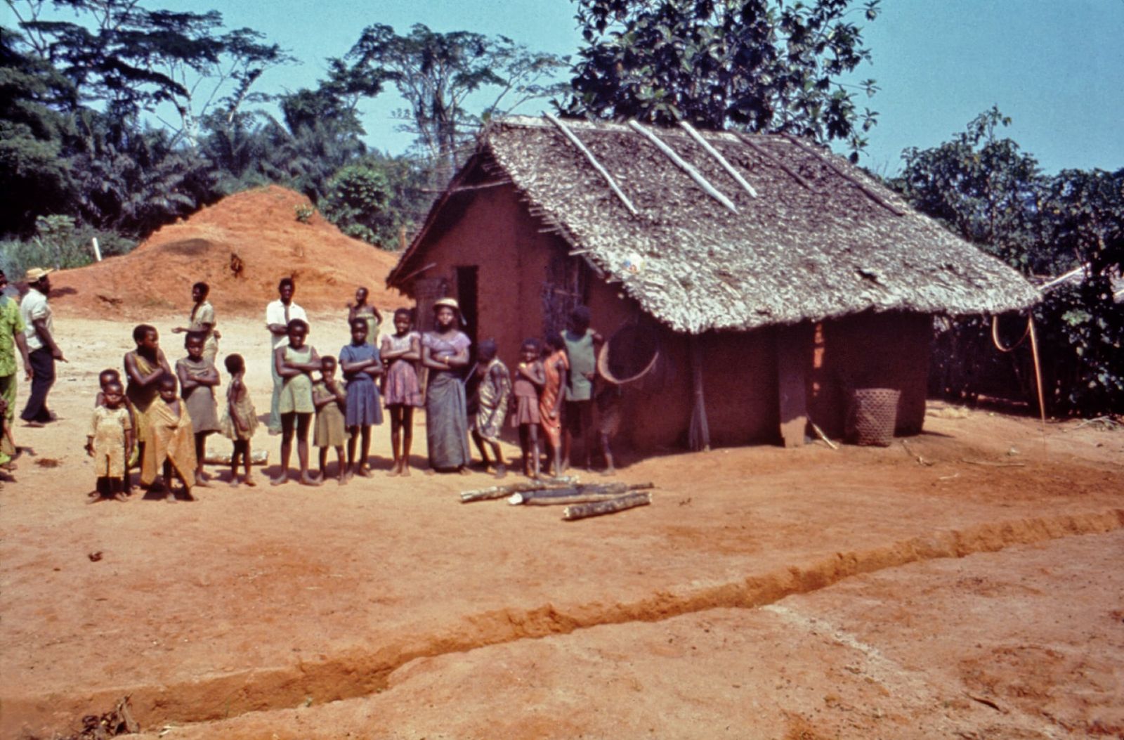 Residents of Yambuku stand outside a thatched mud-brick house in a forest clearing.