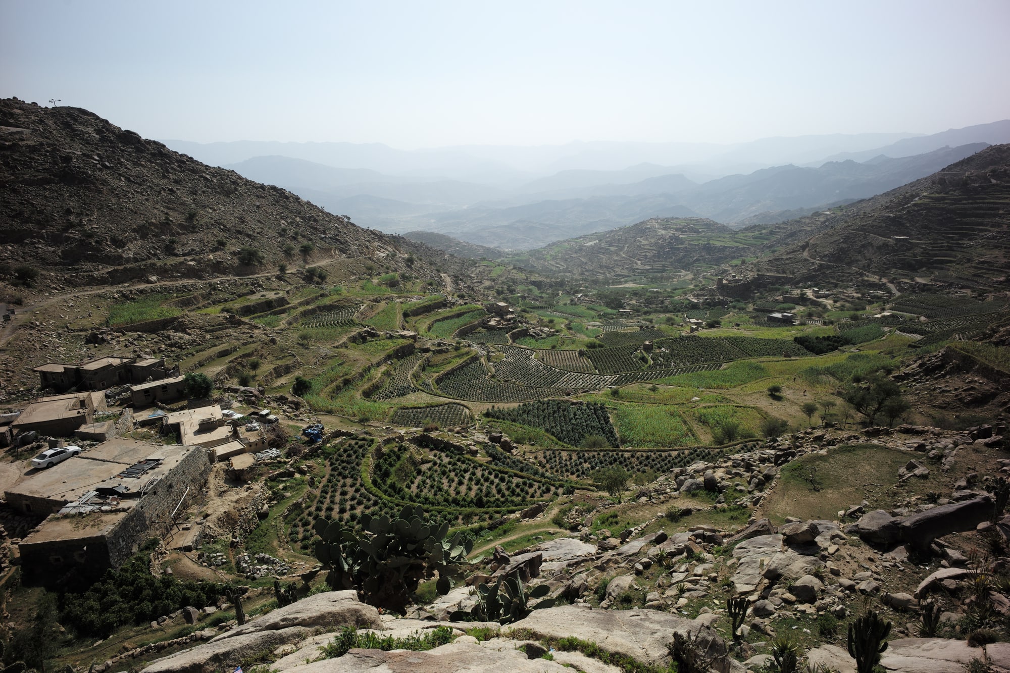 Terraced green fields in a valley between steep, rocky mountains, with stone houses on the slopes.