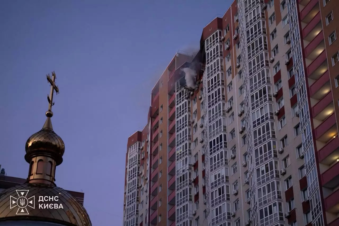 Smoke rising from a damaged upper floor of a tall apartment block in Kyiv, with a church dome in the foreground