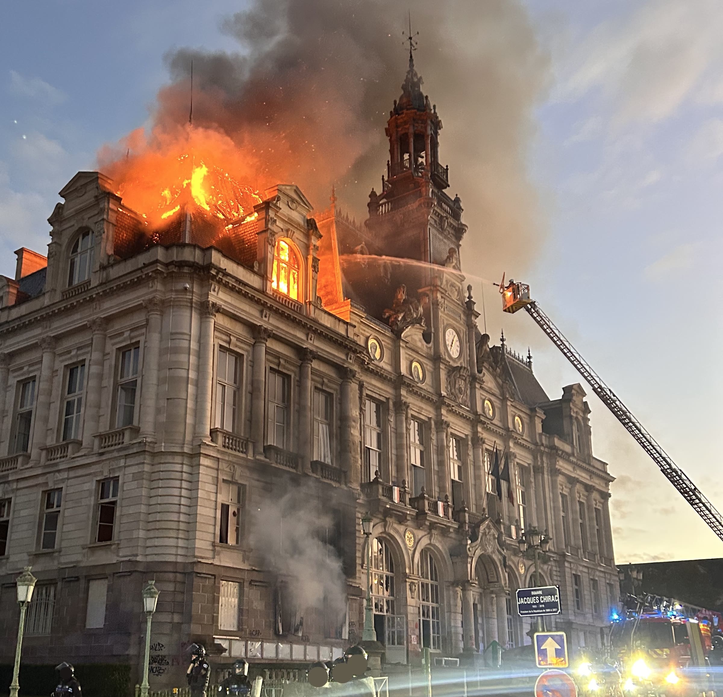 The 19th-century city hall in Limoges in flames at dusk, smoke pouring from its roof as a fire engine ladder reaches towards it