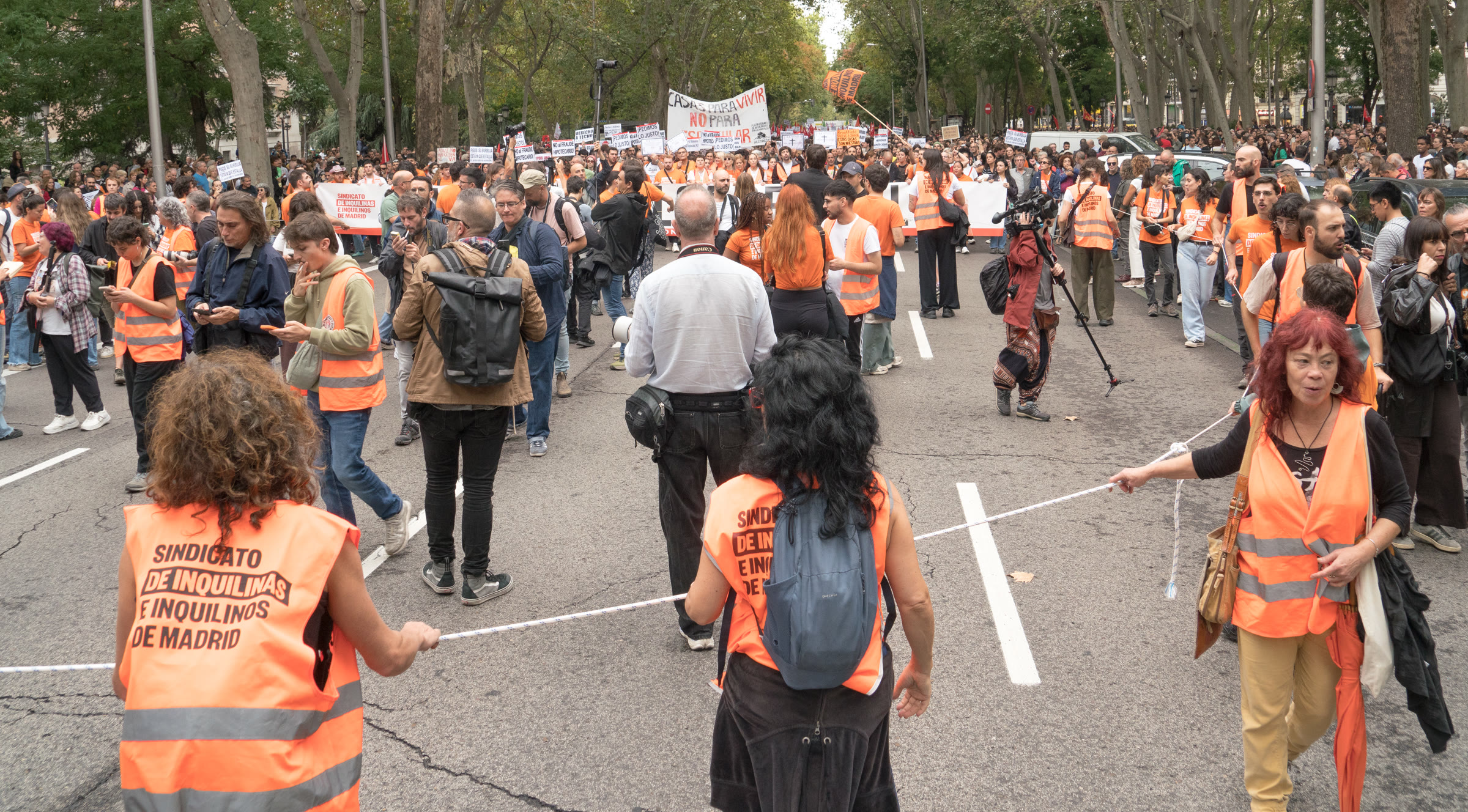 Marchers in orange tenants' union vests hold a rope line along a Madrid avenue packed with protesters