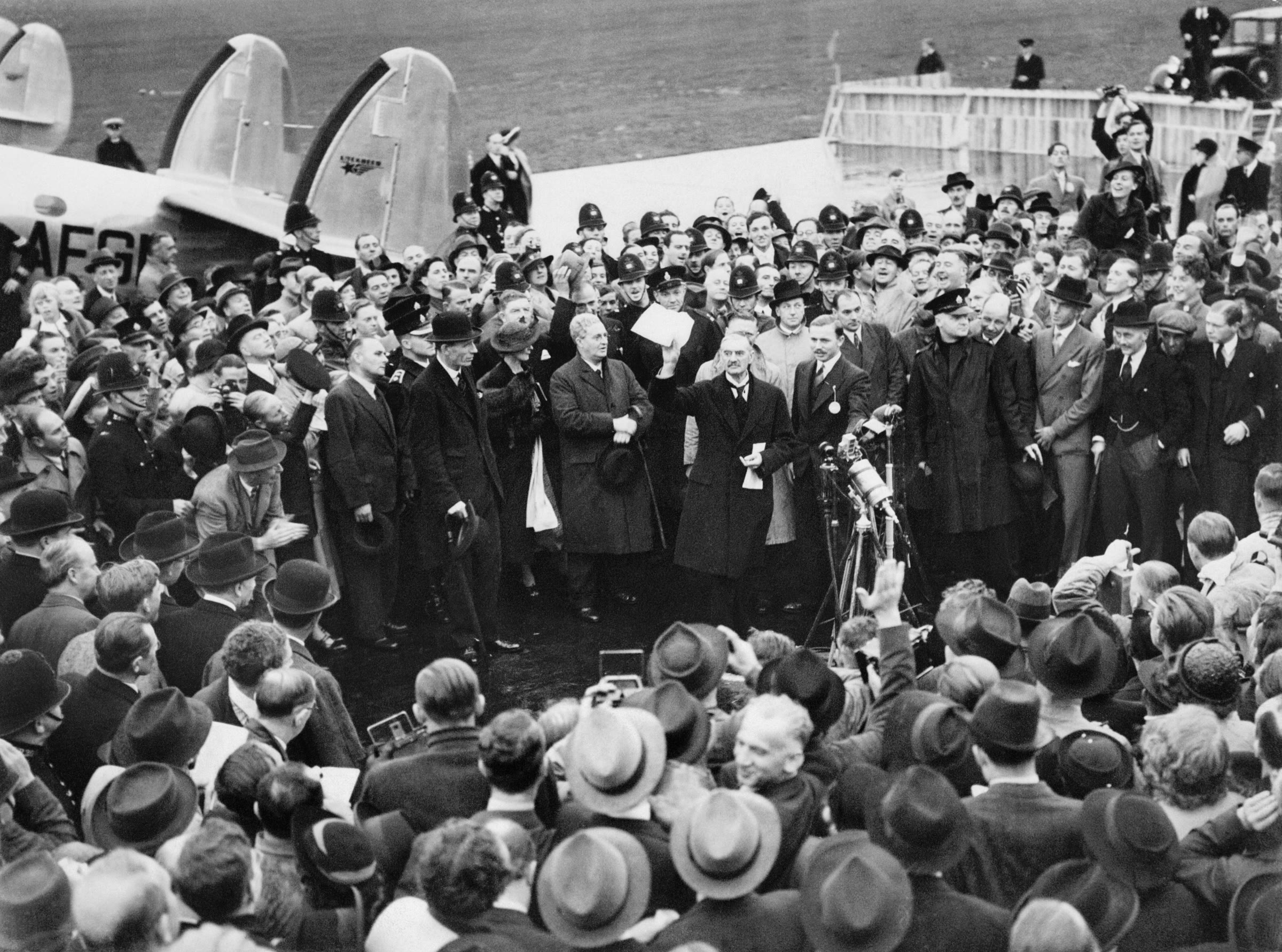 Neville Chamberlain holds up the paper signed with Hitler as he speaks to a crowd at Heston aerodrome on 30 September 1938.