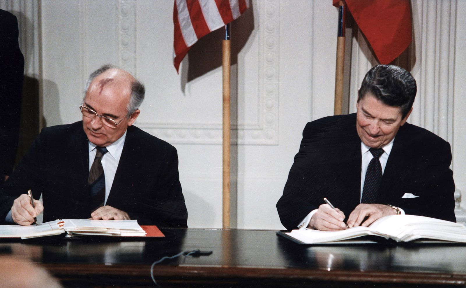 Ronald Reagan and Mikhail Gorbachev sit side by side at a table in the White House signing the INF Treaty, 8 December 1987.