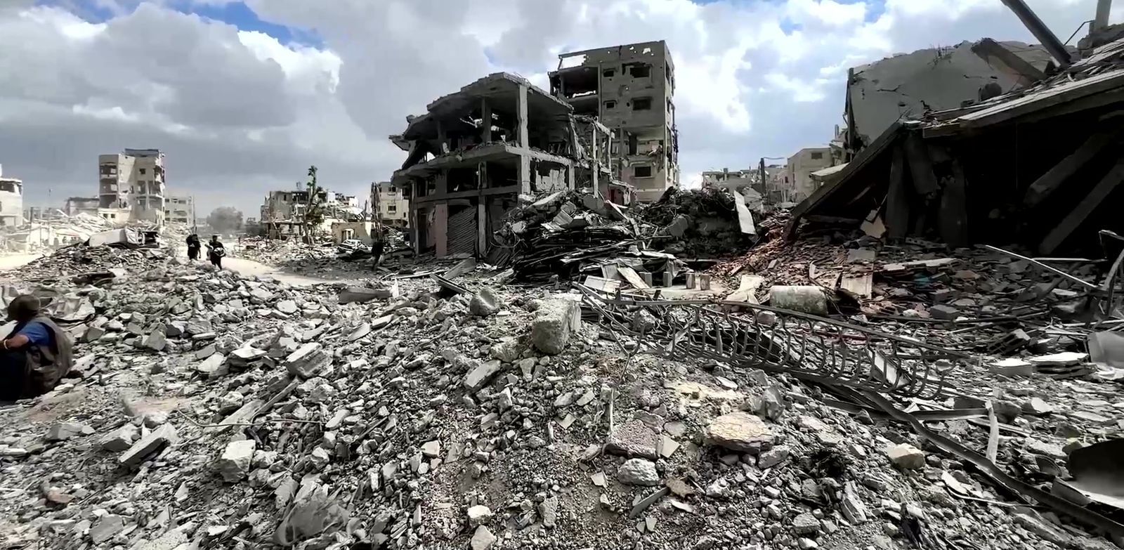 People walking along a street of rubble between destroyed apartment buildings