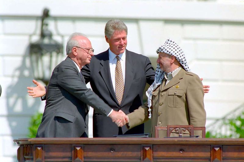 Yitzhak Rabin and Yasser Arafat shaking hands, with Bill Clinton standing between them