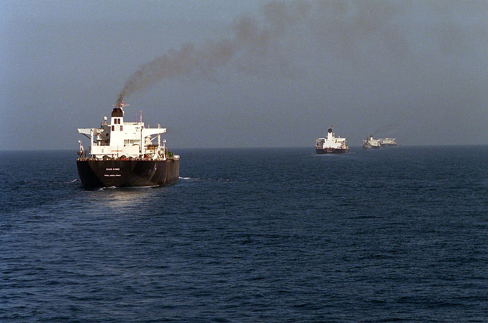 A tanker at sea with other ships of a convoy on the horizon