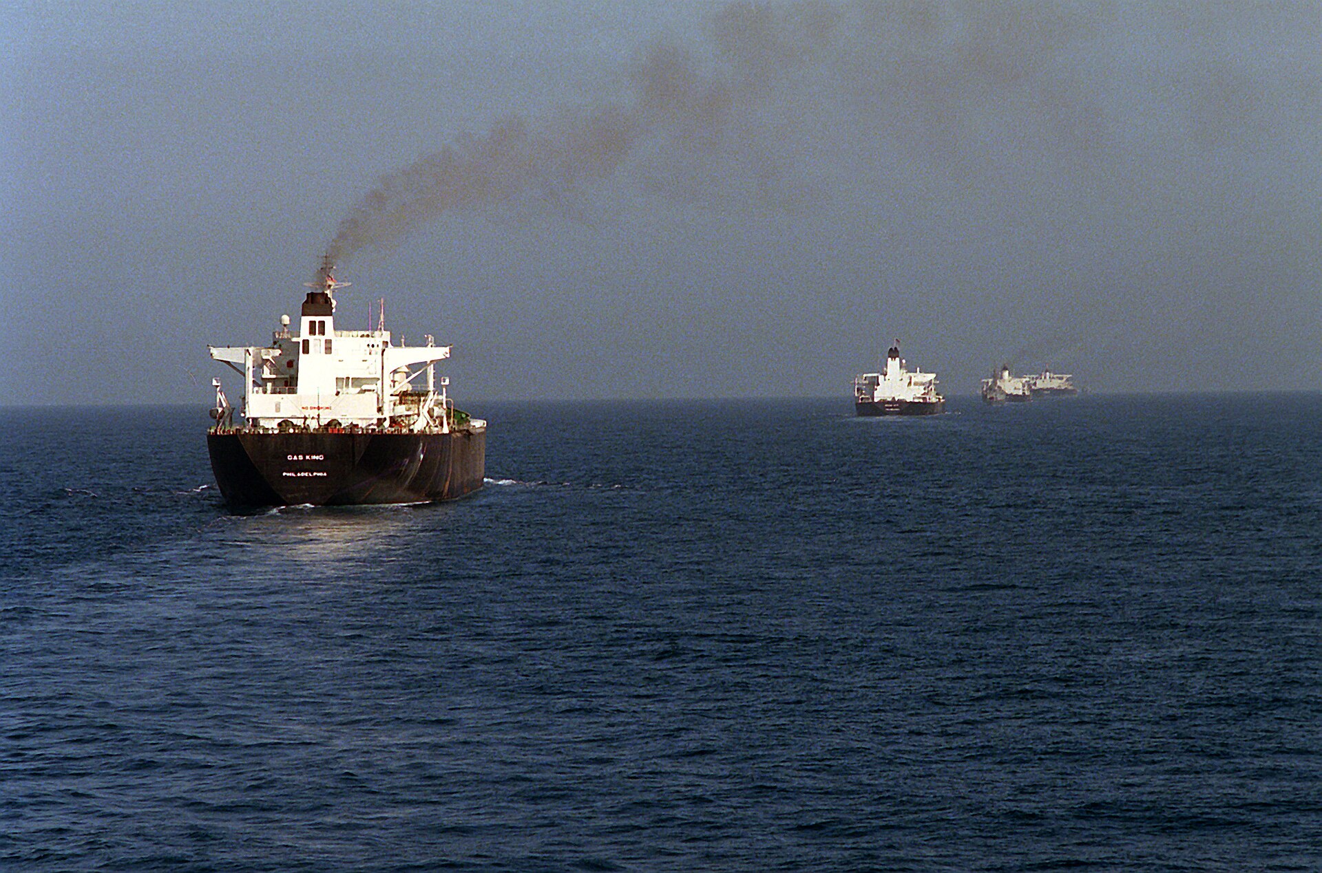 A tanker at sea with other ships of a convoy on the horizon