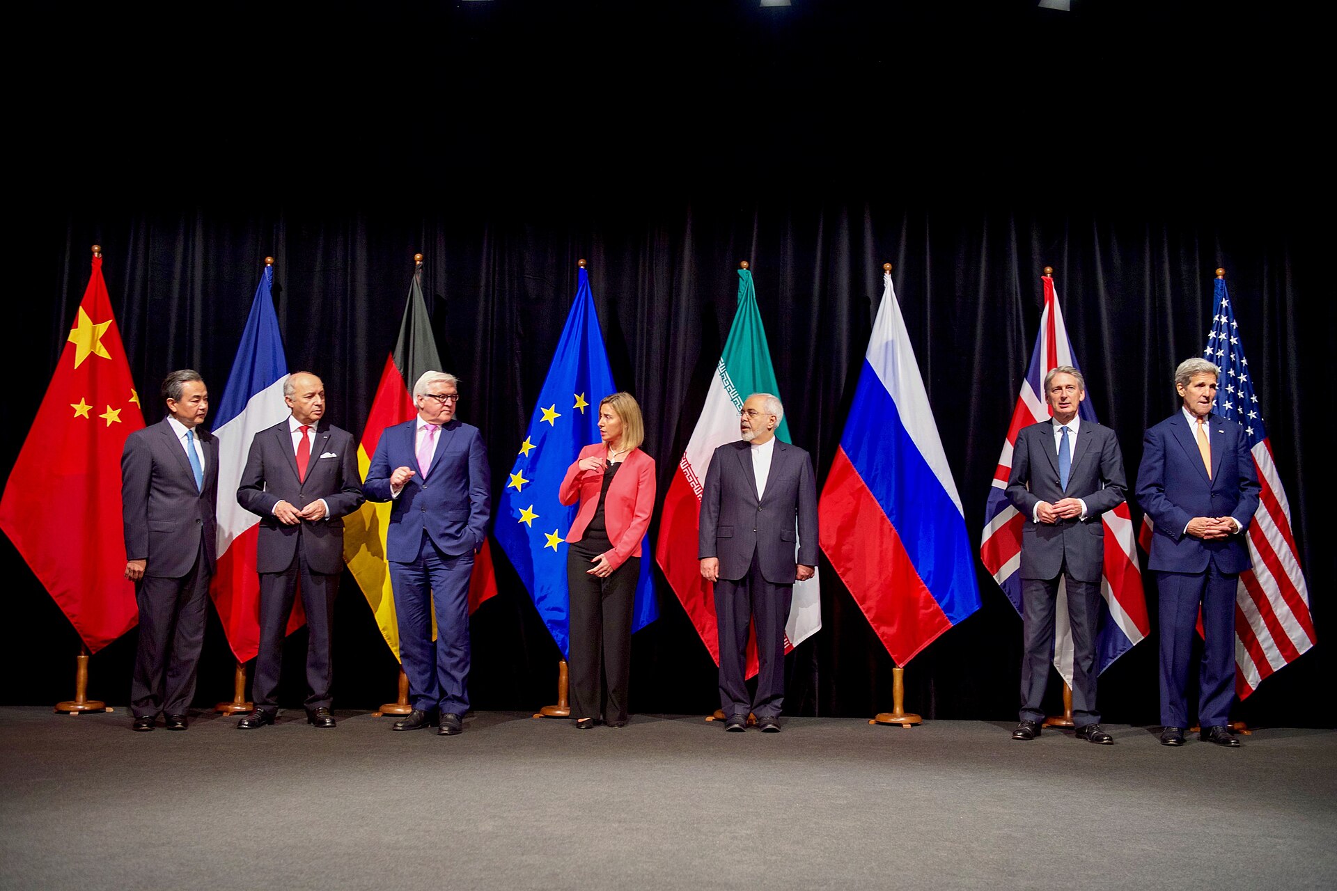 Eight foreign ministers and officials standing in a row in front of their national and EU flags