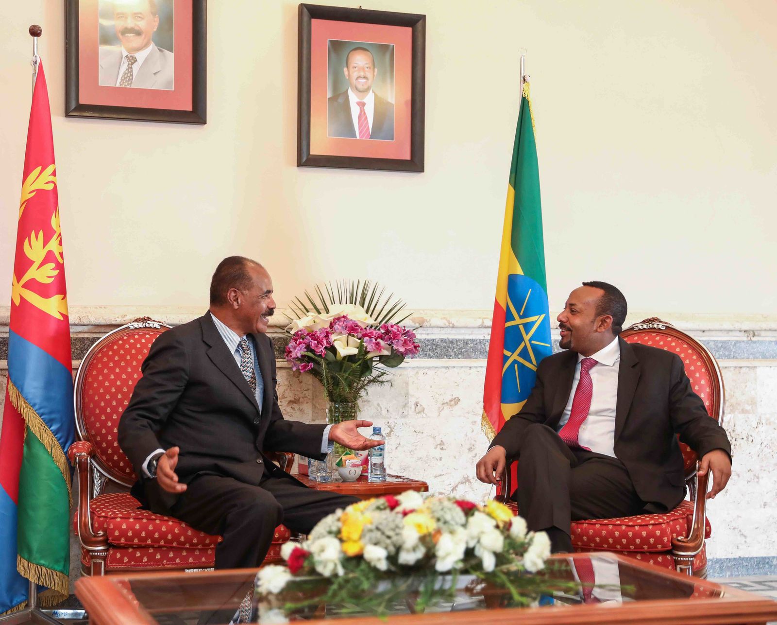 Isaias Afwerki and Abiy Ahmed talking in armchairs between Eritrean and Ethiopian flags
