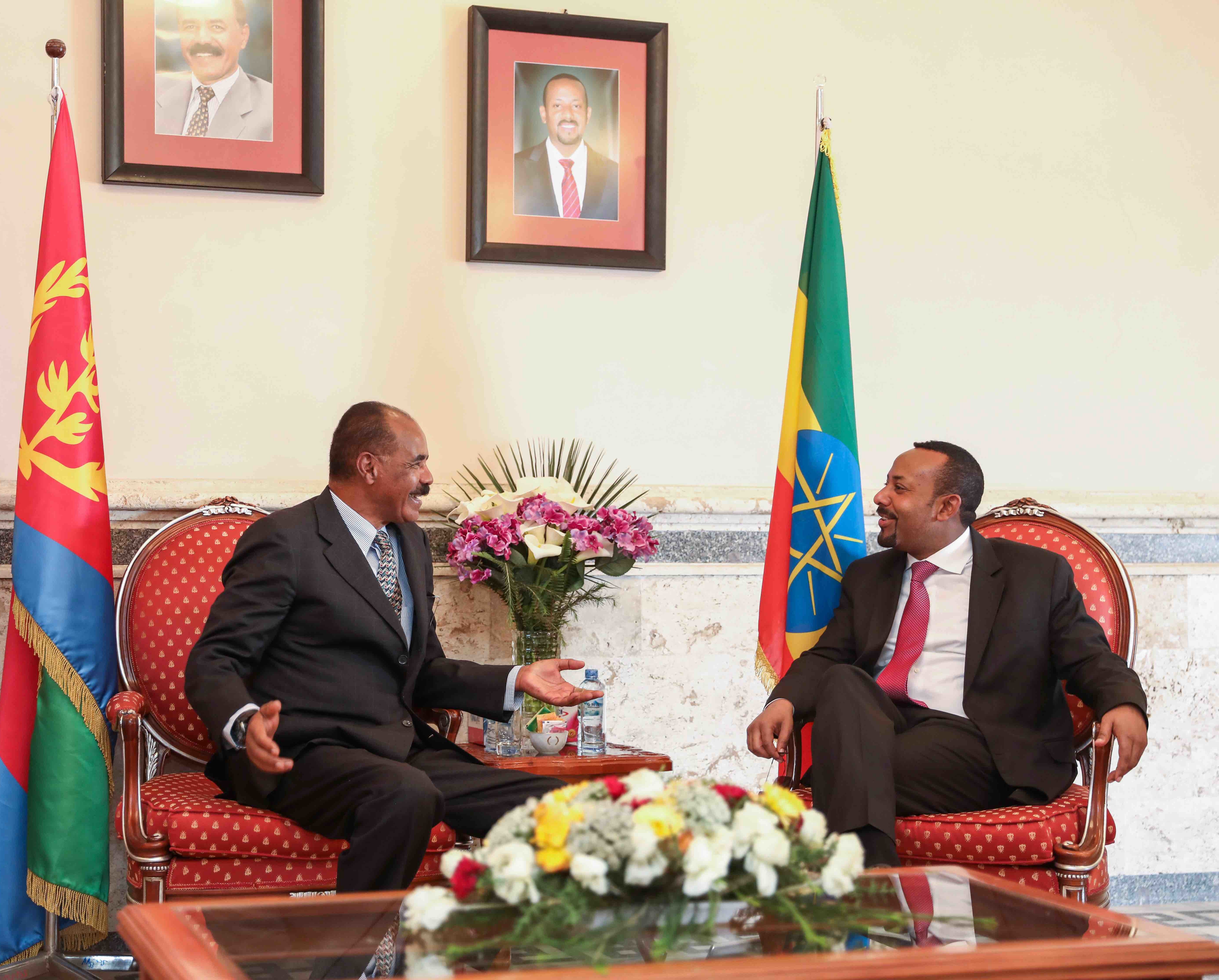 Isaias Afwerki and Abiy Ahmed talking in armchairs between Eritrean and Ethiopian flags