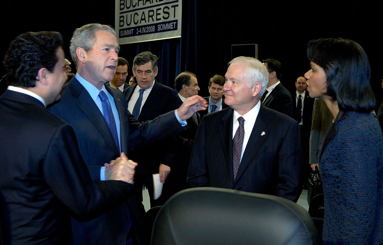 President George W. Bush talking with other delegates at a summit, beneath a sign reading Bucharest Summit 2-4.IV.2008