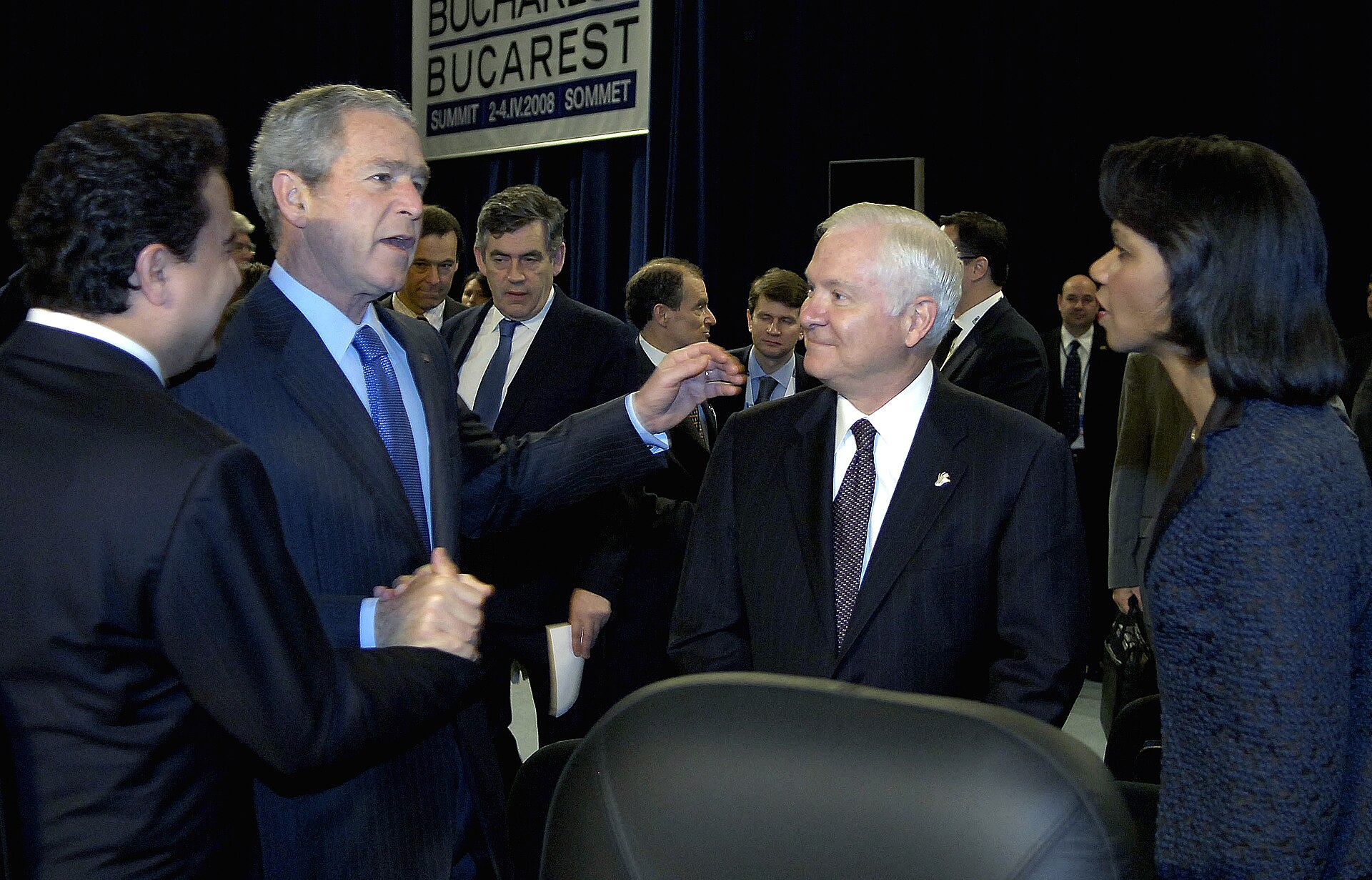 President George W. Bush talking with other delegates at a summit, beneath a sign reading Bucharest Summit 2-4.IV.2008