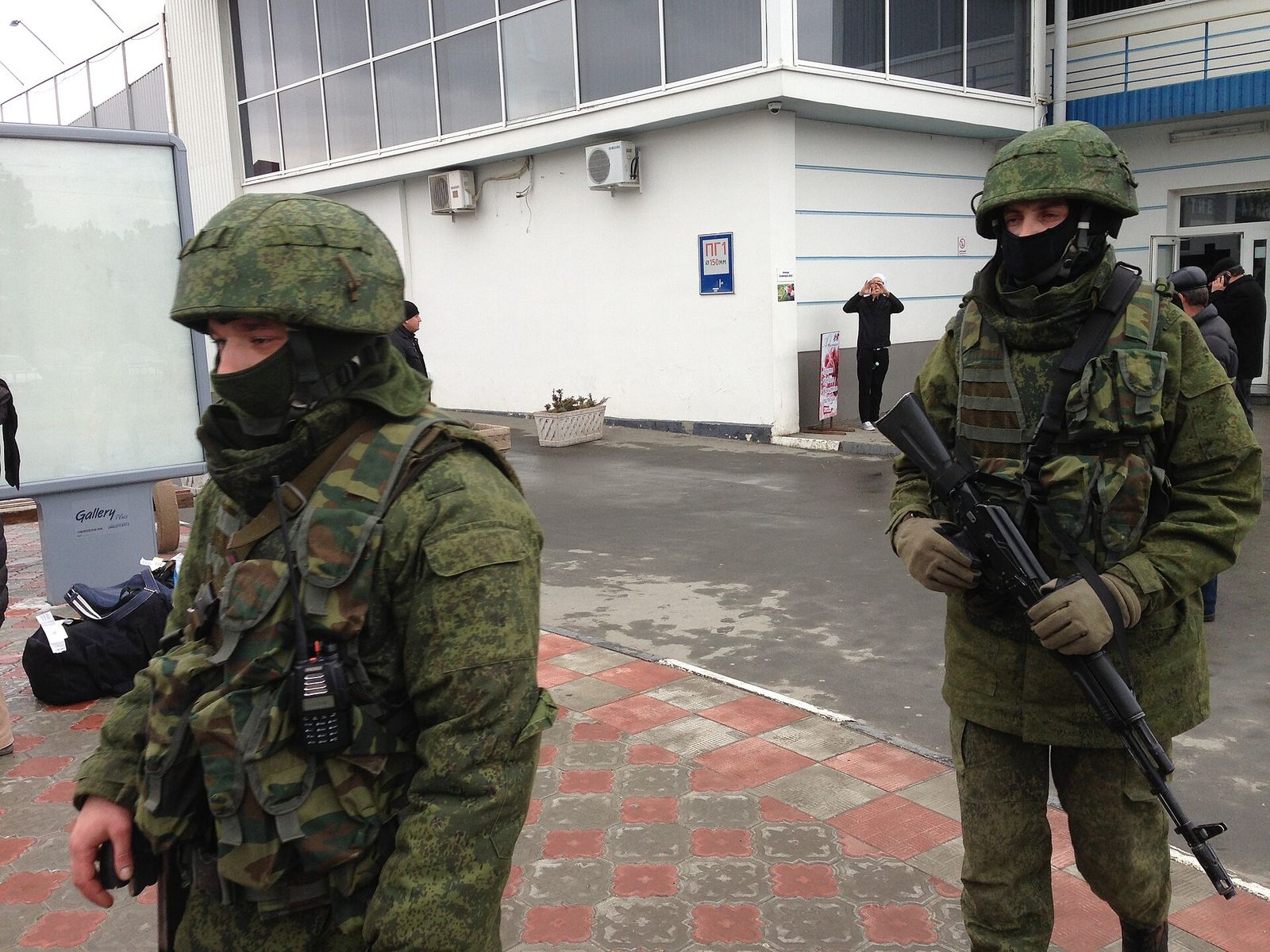 Two armed men in camouflage without insignia standing outside an airport building