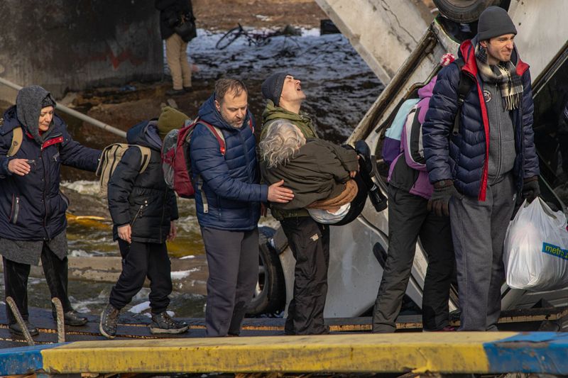 Civilians crossing a damaged area of the Irpin river on foot, carrying belongings